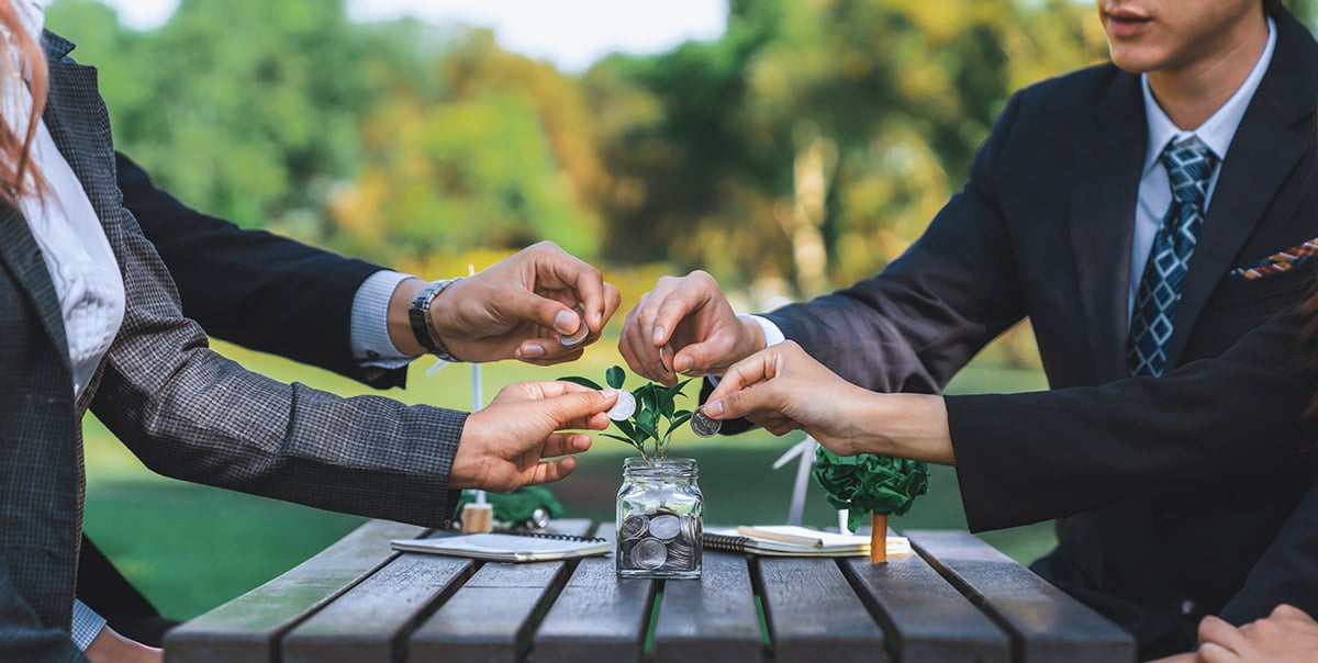 Group of business professionals investing coins in a jar with a plant, illustrating the impact of private equity on the circular economy.