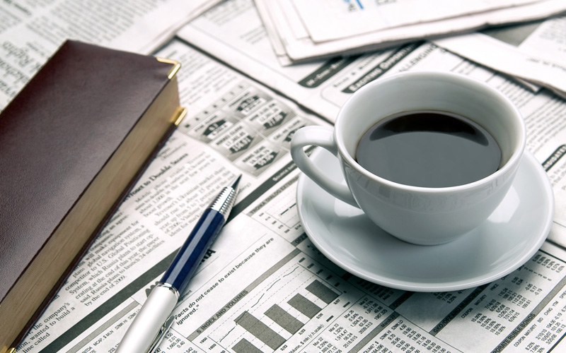 Image of coffee cup, planner, and pen resting on the finance section of a newspaper.