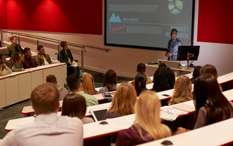 Image of a man teaching a class on market research to a group of young students.